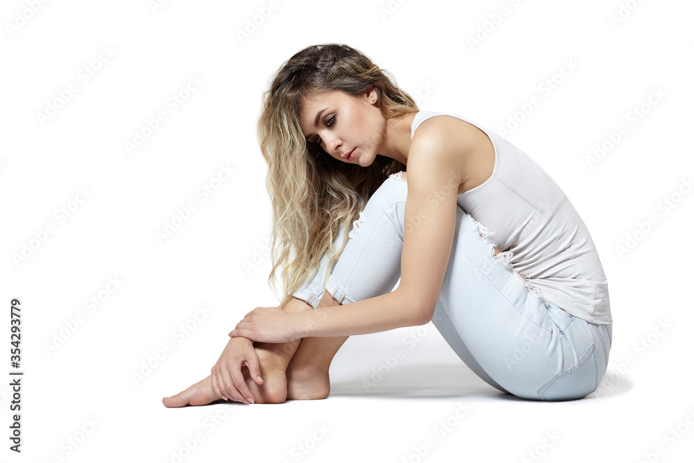 Young pretty in jeans and shirt woman sitting on gray background