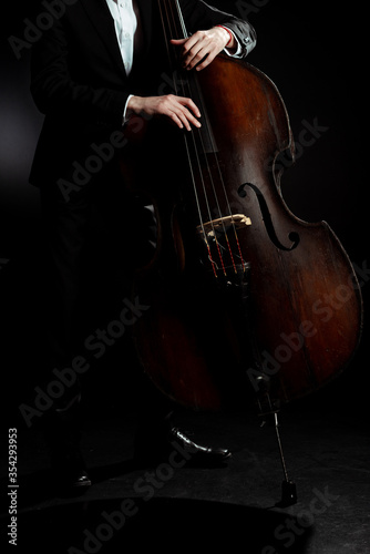 cropped view of professional musician playing on double bass on dark stage