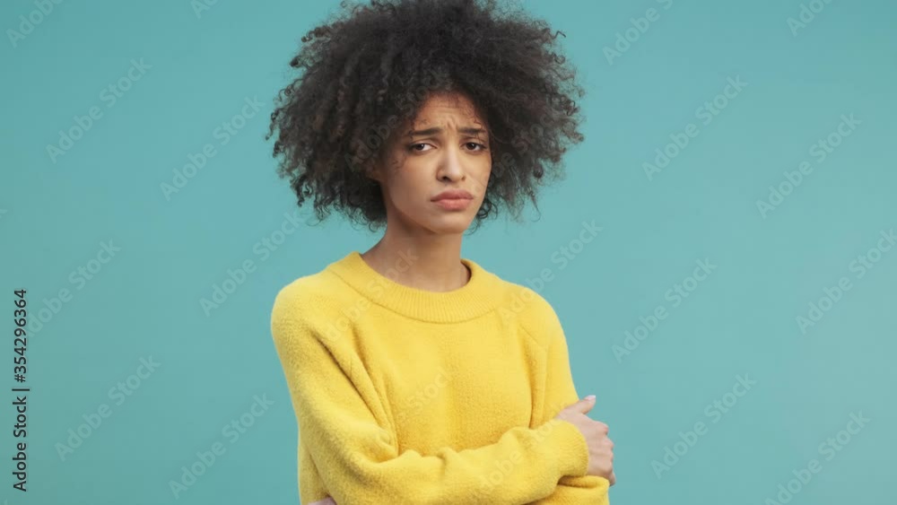 A displeased young african american woman with curly hair is showing NO gesture while shaking her hand isolated over blue wall background in studio A displeased young african american woman with curly hair is showing NO gesture while shaking her hand isolated over blue wall background in studio