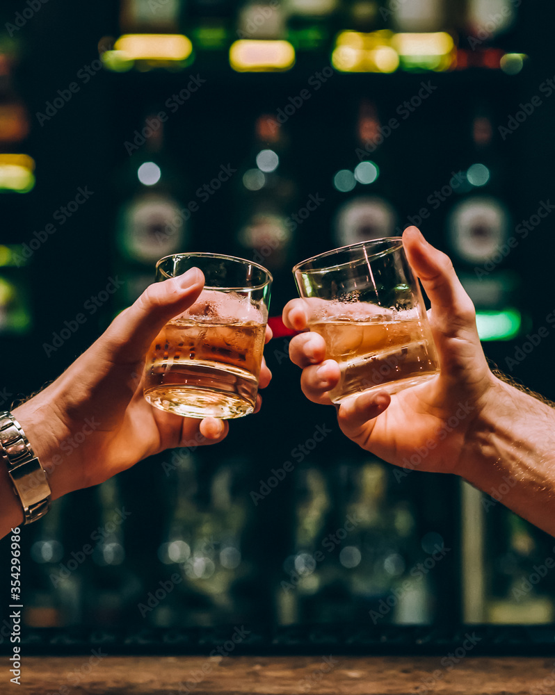two guys clink glasses with whiskey at the bar - obrazy, fototapety, plakaty 