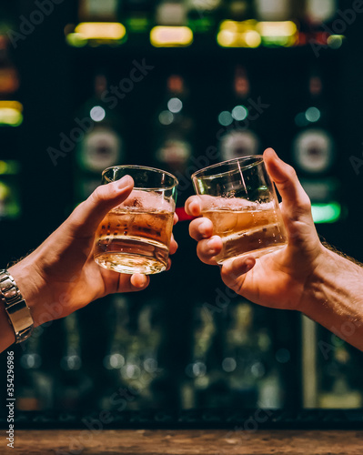 Tela two guys clink glasses with whiskey at the bar