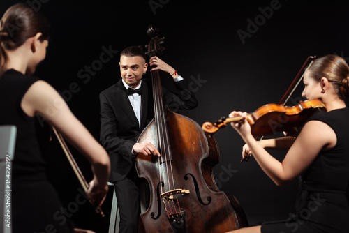 trio of happy musicians playing on double bass and violins isolated on black