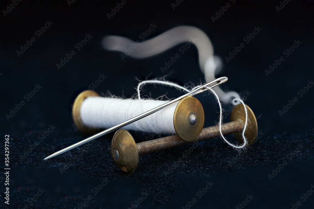 Single spool of sewing thread shot against a dark background, needle visible in shot Single spool of sewing thread shot against a dark background, needle visible in shot