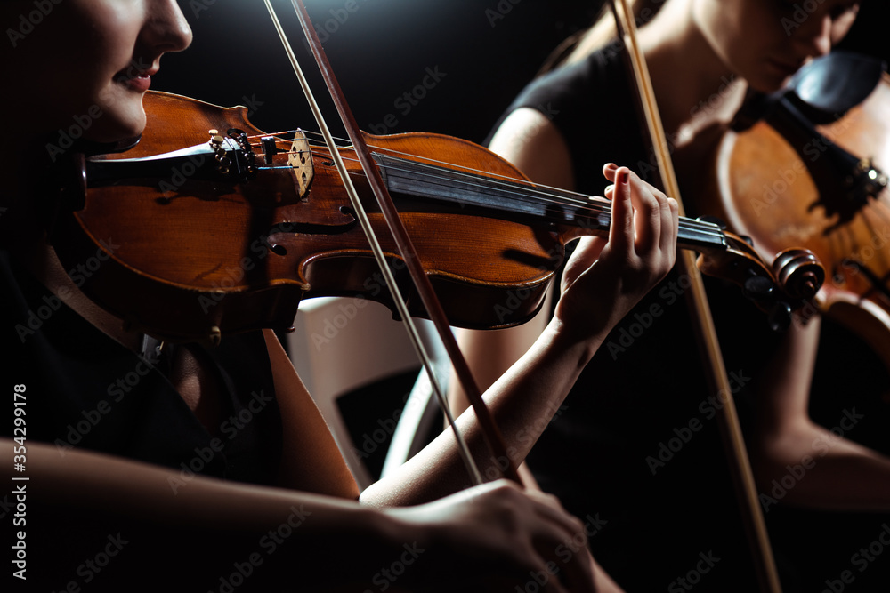 cropped view of two female professional musicians playing on violins on dark stage - obrazy, fototapety, plakaty 