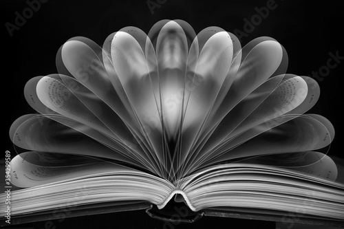 A black and white photo of a book with folded, fanned pages with a double exposure effect for artistic purposes.  Light painting technique shot against black background