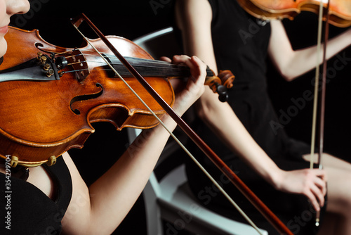 cropped view of two female professional musicians playing on violins on dark stage