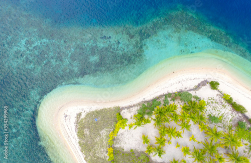 Top view of small isolated tropical island with white sandy beach and blue transparent water