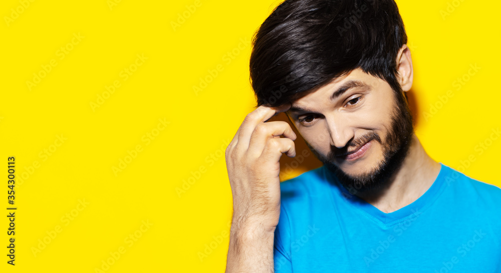 Studio close-up portrait of young guy feeling doubt emotions, wearing blue shirt, holding hand on head, background of yellow color with copy space. Studio close-up portrait of young guy feeling doubt emotions, wearing blue shirt, holding hand on head, background of yellow color with copy space.