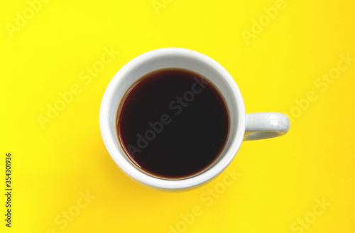 Black coffee in a white cup isolated on a yellow background. Selective focus. Top view