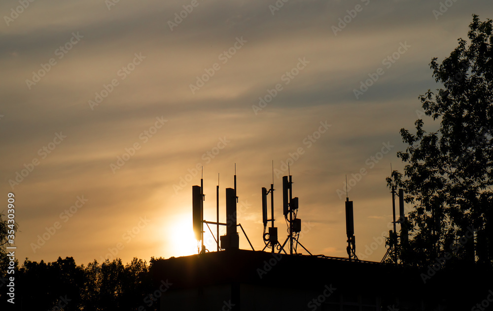 antennas of cellular communication and Internet connections on the roof of buildings against the sunset sky