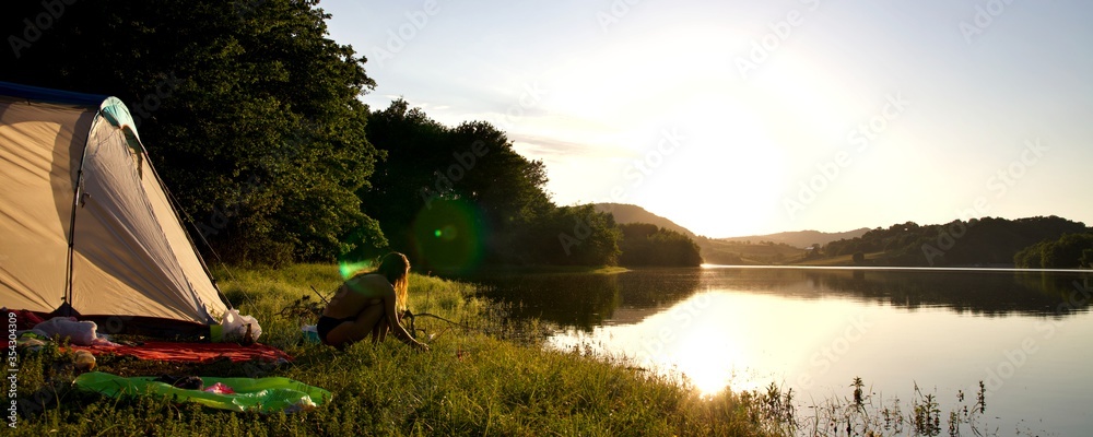 Camping sauvage bivouac coucher de soleil - tente campement jeune femme feu - tourisme détente calme vacances aventure - obrazy, fototapety, plakaty 
