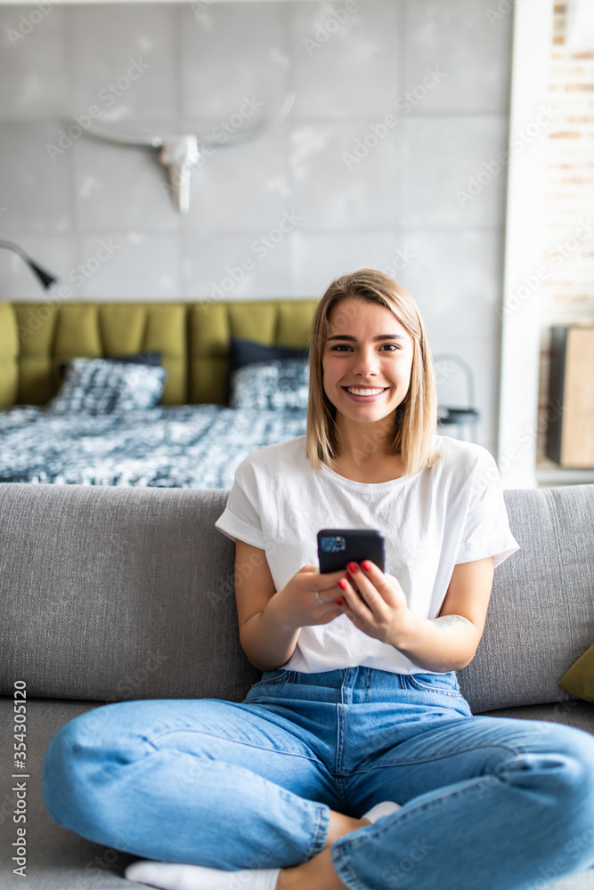 Portrait of happy young woman with mobile phone sitting on couch at home