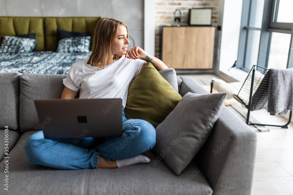 Young woman using a laptop while relaxing on the couch Young woman using a laptop while relaxing on the couch