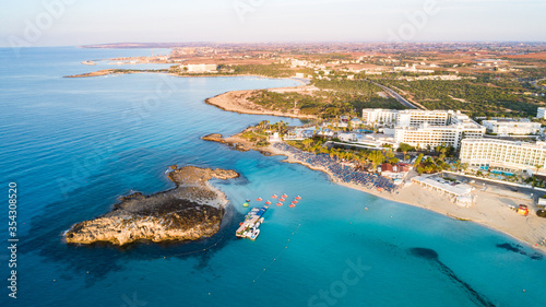 Aerial bird's eye view of famous Nissi beach coastline, Ayia Napa, Famagusta, Cyprus.Landmark tourist attraction islet bay at sunrise with golden sand, sunbeds, sea restaurants in Agia Napa from above