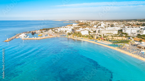 Aerial bird's eye view of Pantachou - Limanaki beach (Kaliva), Ayia Napa, Famagusta, Cyprus. Bay with golden sand, small fishing port, sunbeds, parasols, sea bar restaurants in Agia Napa, from above. © f8grapher