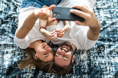 Selfie. Top view of beautiful young loving couple lying in bed and making selfie on the phone
