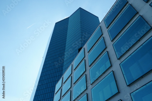 a facade of a modern corporate building with large square window in upward perspective with sky on the background and another corporate tower building behind it 