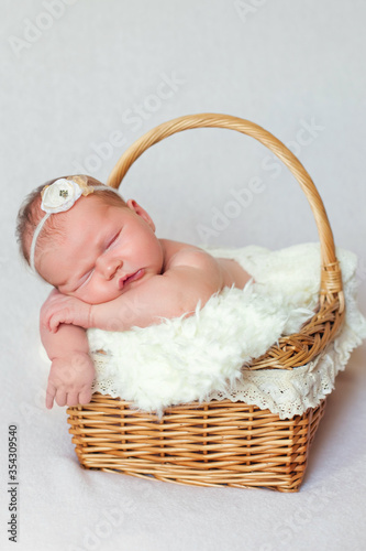 Close-up of an adorable newborn baby sleeping in a wicker basket. Sweet baby lies in a basket and smiles in his sleep. Isolated on a white background Studio. Sleeping girl with a flower on her head.