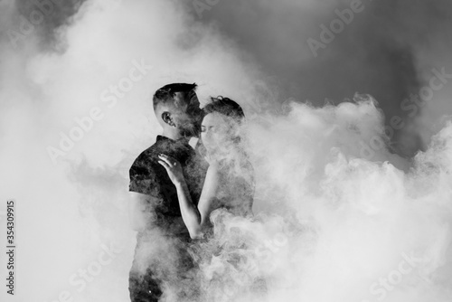 guy and a girl in black clothes hug inside a smoke