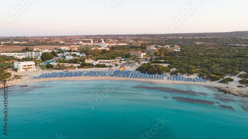 Aerial bird s eye view of Landa beach  Ayia Napa  Famagusta  Cyprus. Landmark tourist attraction golden sand bay at sunrise with sunbeds  sea restaurants at Makronissos and nissi  Agia Napa from above