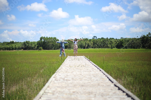 A woman standing on a wooden bridge in a rice field