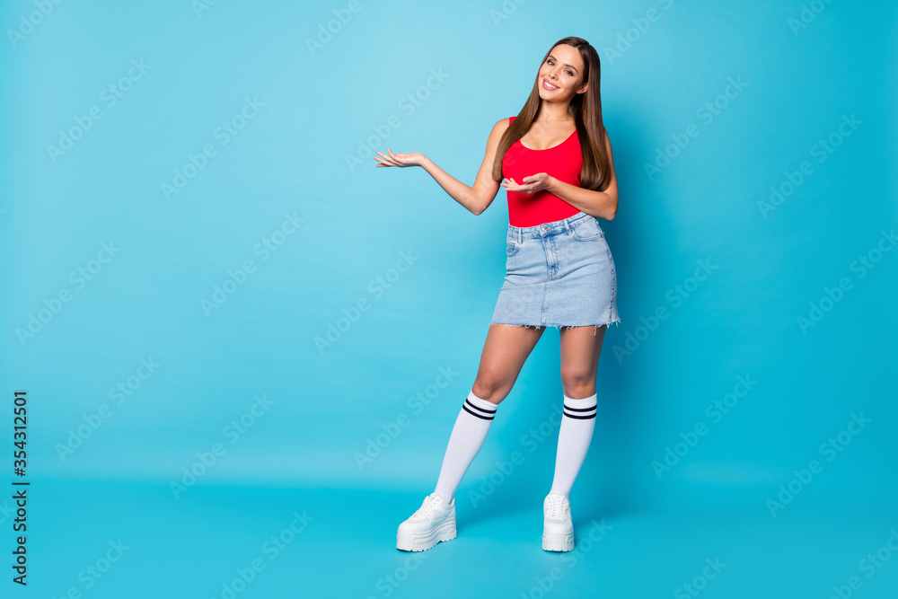 Full size photo of positive cheerful cool confident girl promoter hold hand present ads promo wear good look socks shoes shine tank-top isolated over blue color background