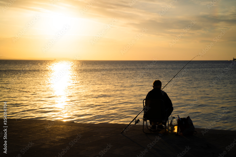 Silhouette of man sitting and fishing peacefully during the sunset