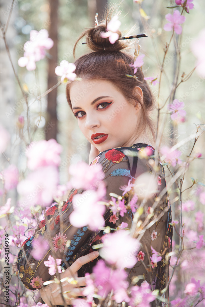 Fototapeta premium A girl dressed in Japanese style in a flowering forest among pink flowers