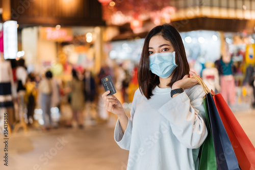woman wearing medical mask and holding credit card at shopping mall for prevention from coronavirus (Covid-19) pandemic. new normal concepts