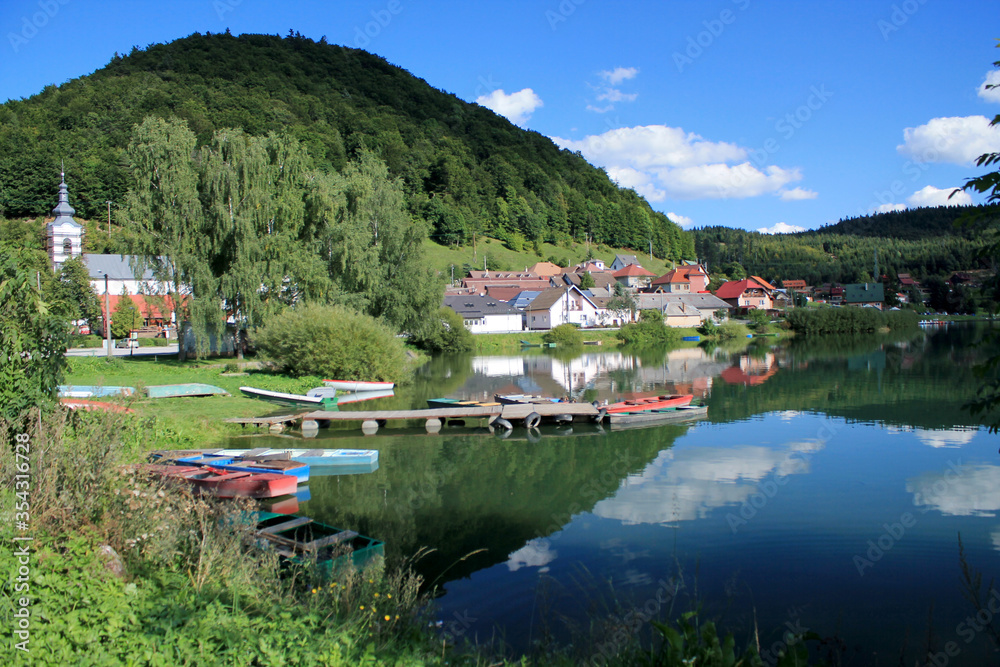 View to mountain, village, lake, boats and reflection of sky and clouds in water.