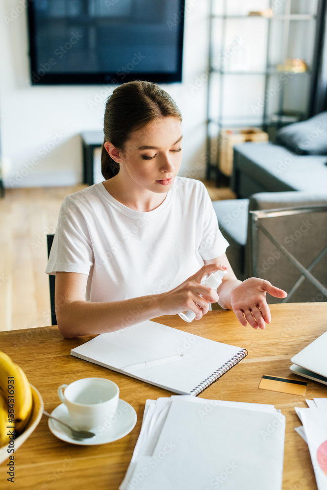 attractive woman holding bottle with hand sanitizer near notebook and cup on table attractive woman holding bottle with hand sanitizer near notebook and cup on table