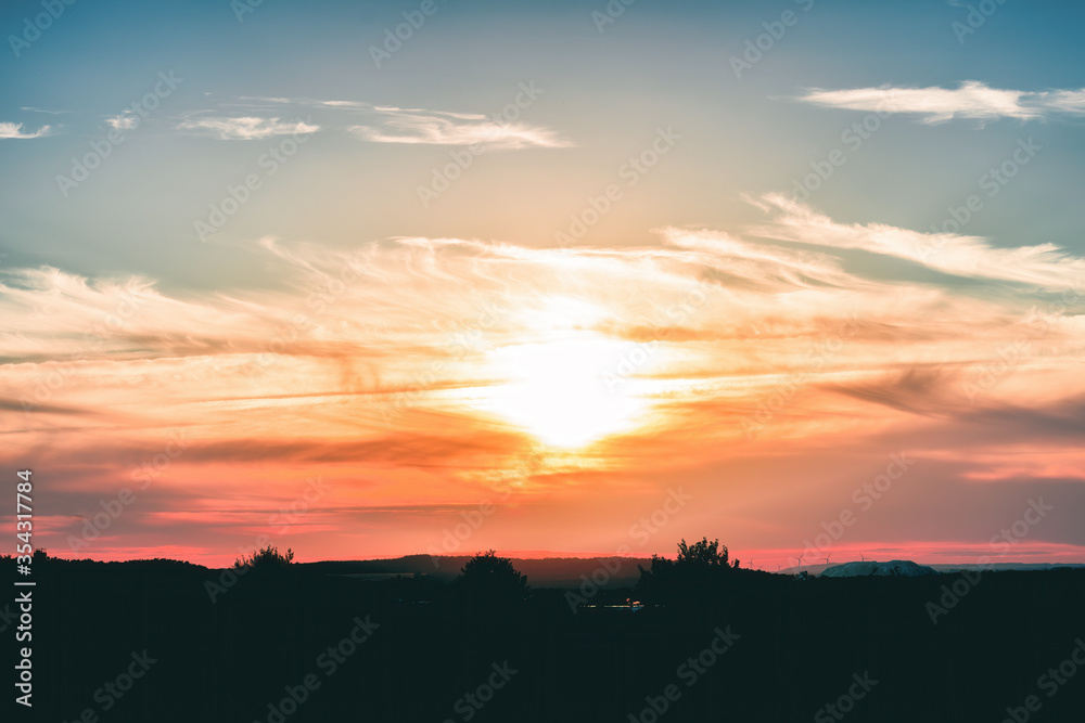 A deep red sunset in the silhouette of mountains and trees