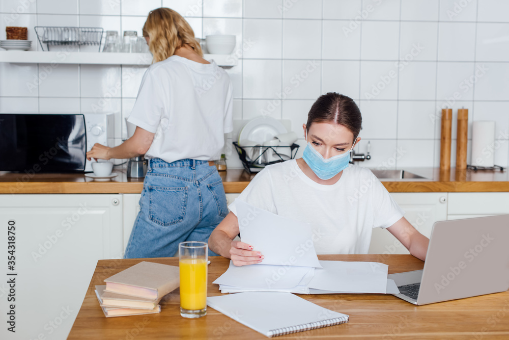 freelancer in medical mask near books, laptop, glass of orange juice and sister freelancer in medical mask near books, laptop, glass of orange juice and sister