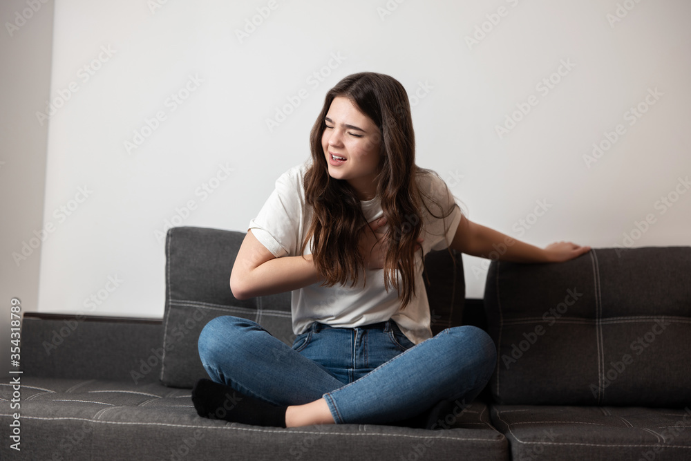 young beautiful brunette woman sitting on the sofa suffering from extreme pain in chest looking desperate, healthcare and medical concept young beautiful brunette woman sitting on the sofa suffering from extreme pain in chest looking desperate, healthcare and medical concept