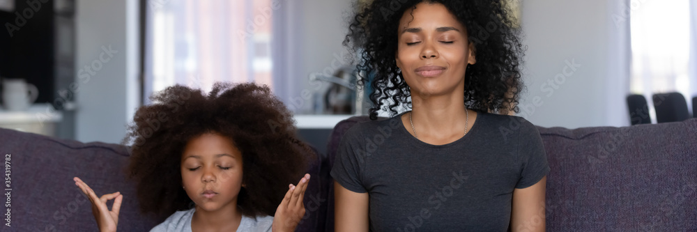 Calm African mother her funny little daughter sit on couch do meditation practice together at home. No stress, teach kid healthy life habits concept. Horizontal photo banner for website header design - obrazy, fototapety, plakaty 