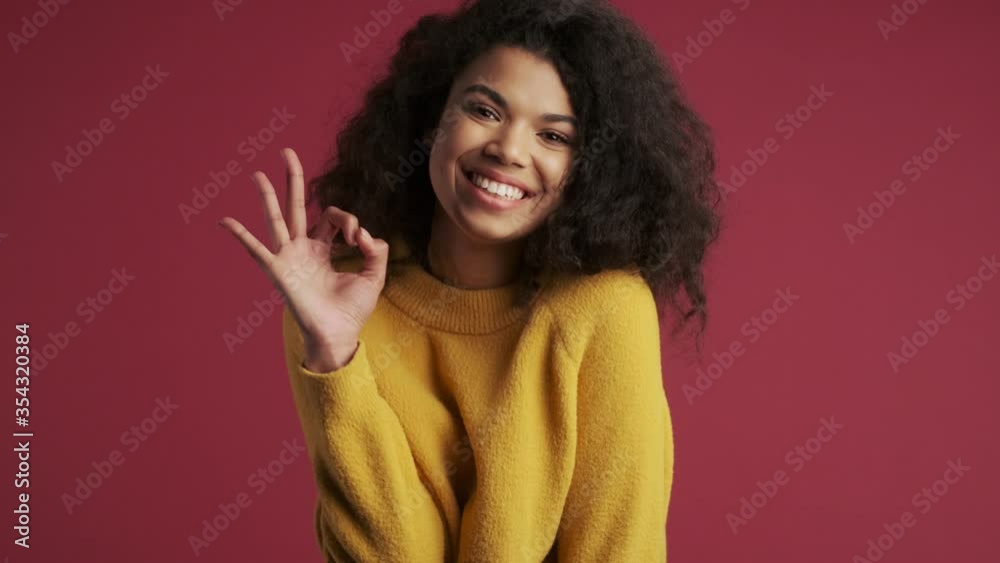 Young pretty positive optimistic african woman isolated over dark red burgundy background showing okay gesture