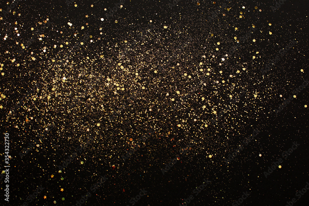 Golden glitter sparkle or stars on black background.