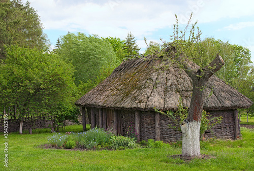 Pereyaslav, Ukraine-May 16, 2020:Landscape view of ancient traditional ukrainian barn with a straw roof and wicker walls. Trees in the background. Concept of historical buildings of ancient Ukraine