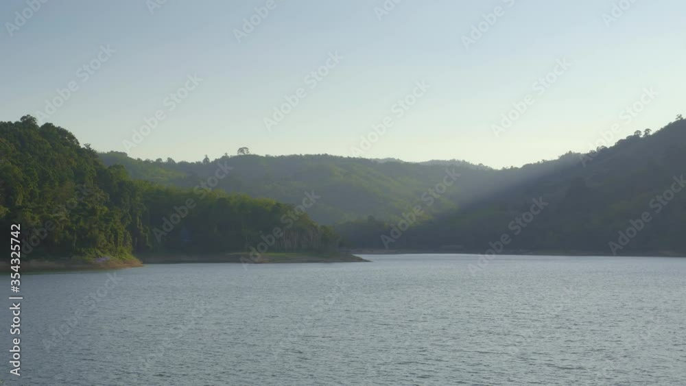View on a lake with green shores and hills are covered with forest in shadow in the evening View on a lake with green shores and hills are covered with forest in shadow in the evening