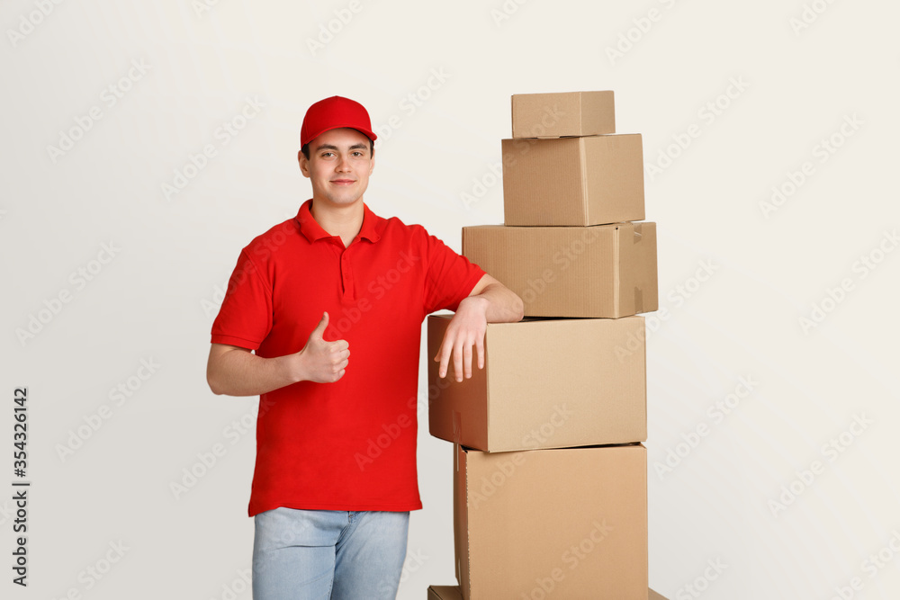 Deliveryman shows sign with hand is good, leaning on cardboard boxes Deliveryman shows sign with hand is good, leaning on cardboard boxes