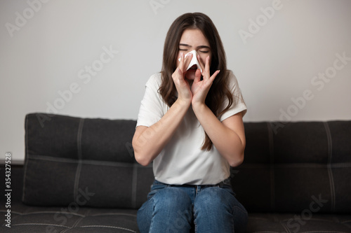 young beautiful brunette woman sitting on the sofa bowing her running nose looking sick, healthcare and medical concept