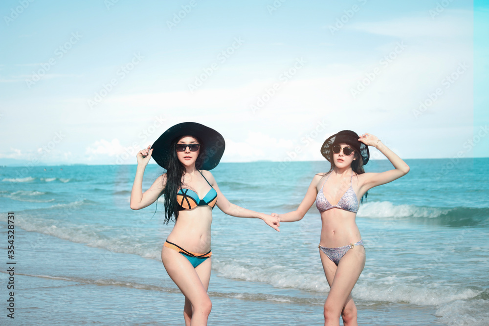 Happy summer holiday vacation, hot sexy beautiful two women in bikini and hat walking, resting and spending time with friend together to relexation on tropical island beach with blue sae Happy summer holiday vacation, hot sexy beautiful two women in bikini and hat walking, resting and spending time with friend together to relexation on tropical island beach with blue sae