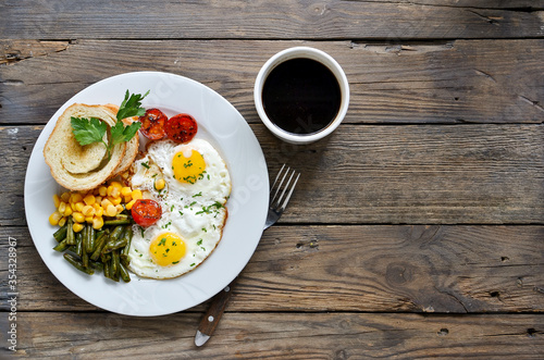 Fried eggs with tomatoes, green beans, corn and toast. English vegetarian breakfast. Top view. Coffee and fried eggs on a wooden tray. Wood background. Free space for text.