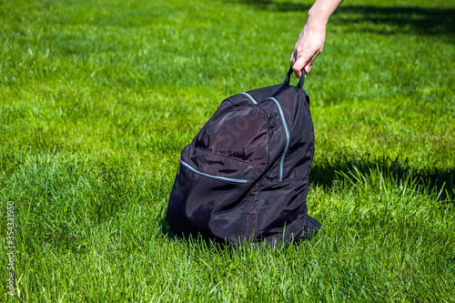 Female hand hold black backpack on green grass. Tourism and Hiking concept