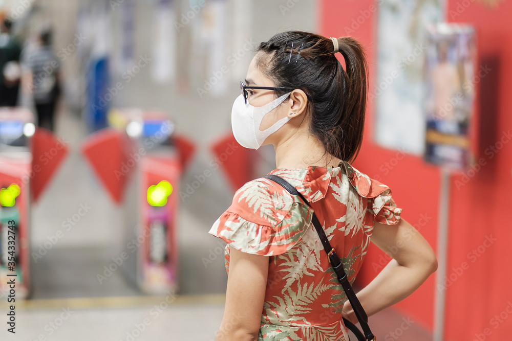 Fototapeta premium young Asian girl wearing Surgical face mask protect coronavirus inflection, Happy tourist woman walking in public subway station. social distancing, new normal and life after covid-19 pandemic