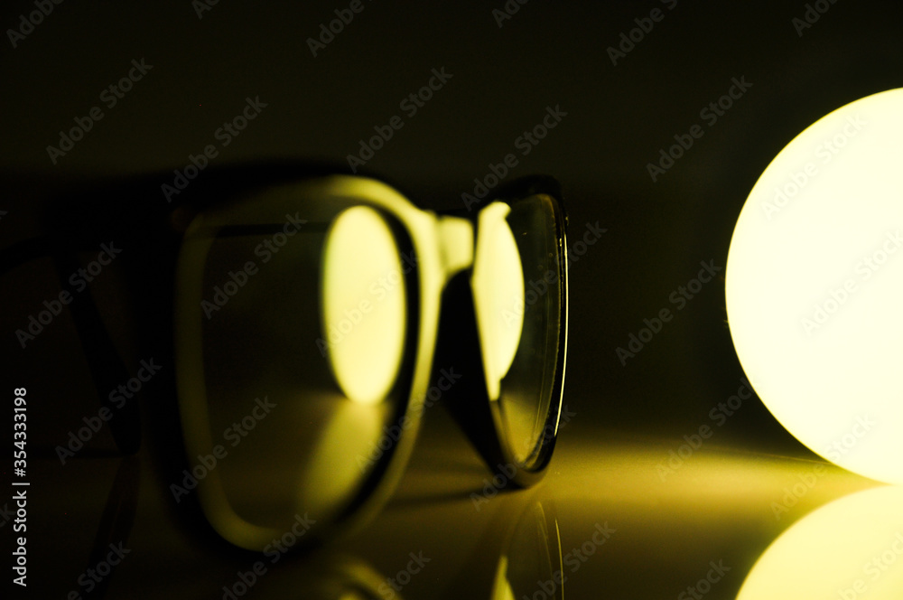 specs spectacles frame placed near light bulb with black background and colorful lighting colours like blue yellow white purple and green