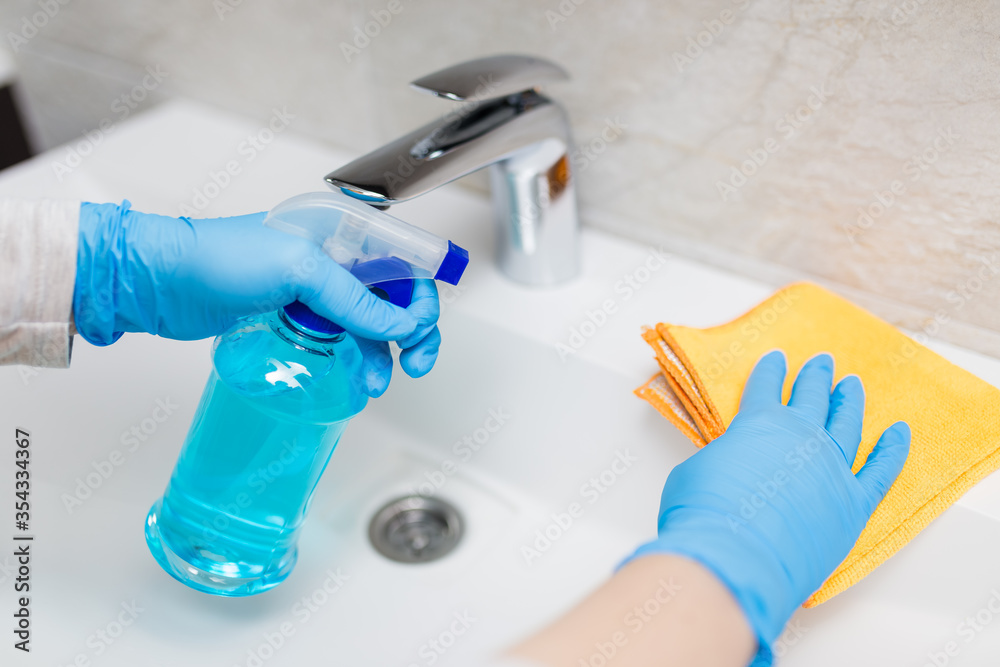 Close up of woman hands in protective gloves cleaning and polishing bathroom sink with cloth and sanitizer spray. Hygiene concept.