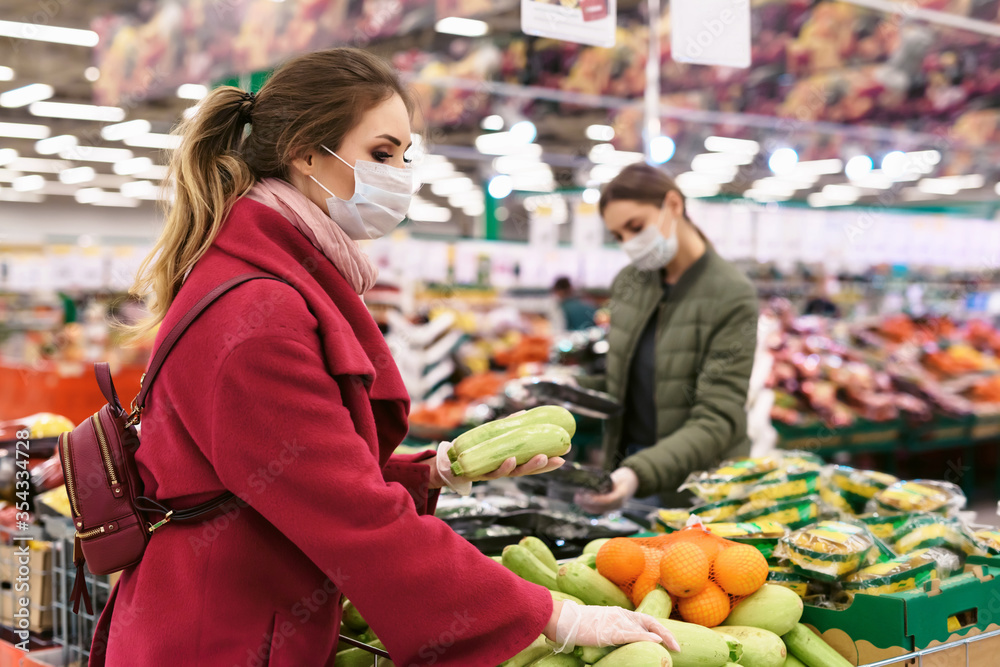 Social distancing in a supermarket. A young woman in a disposable facial mask buying fruits and vegetables and putting them in a grocery basket. Shopping during the Coronavirus Covid-19 epidemic 2020
