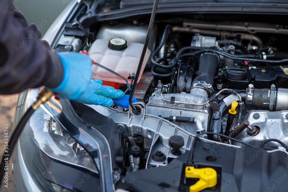 A worker in a car wash washes a car engine. The worker wears blue rubber sneakers. Car wash. Copy Space.