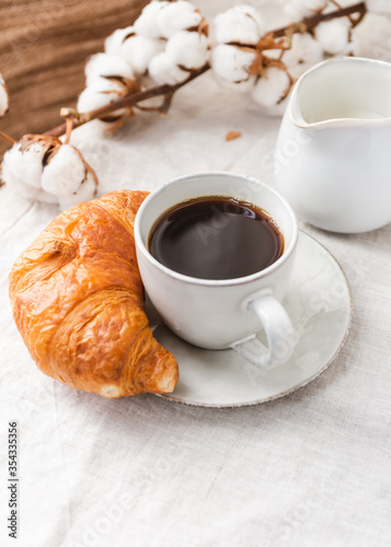 Cup of espresso coffee with croissant on a table with cotton branch.